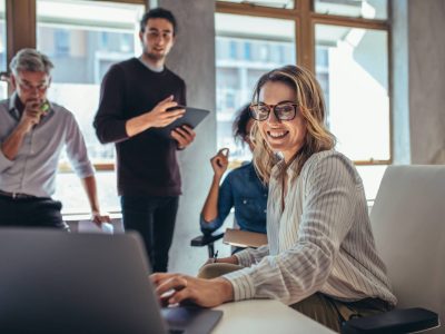 Female entrepreneur working on laptop and explaining strategy to attract followers to online web store while having meeting with colleagues in office